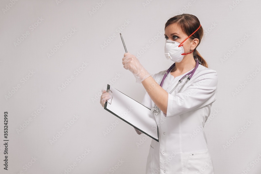 Young beautiful woman doctor in a respirator in a white coat on a light background. Young beautiful woman doctor in a respirator in a white coat on a light background.