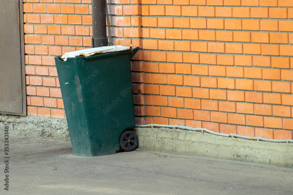 green trash can on wheels near a brick wall green trash can on wheels near a brick wall