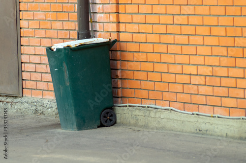 green trash can on wheels near a brick wall