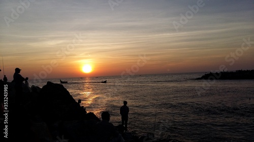 A silhouette landscape image of people watching sunset on a beach with fishing boats in Kerala, India. © Pankaj
