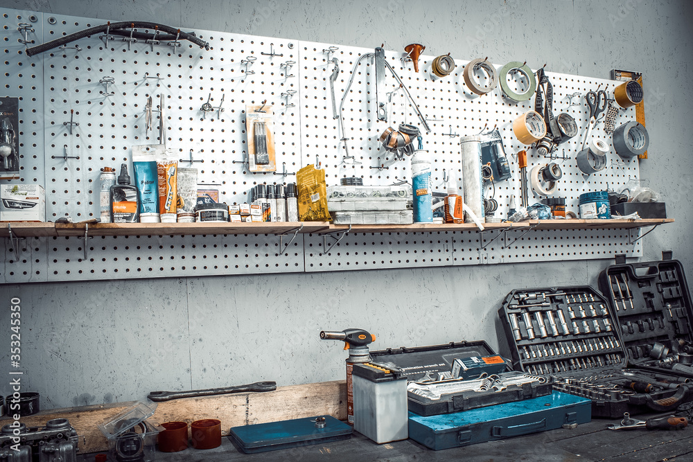 Moto workshop with hand tools. Workbench with sets of keys, screwdrivers,  ploskobets, electrical tape, duct tape on the wall. Table with motorcycle  parts, vise. Workspace for a joiner, auto mechanic Stock Photo