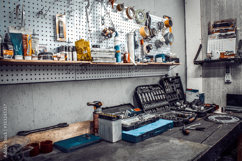 Inside the workshop. Large workbench and tools for working on the table close-up. Workspace for mechanic with wrenches, pliers on a metal wall. Garage for motorcycle repair, car service station. - obrazy, fototapety, plakaty 