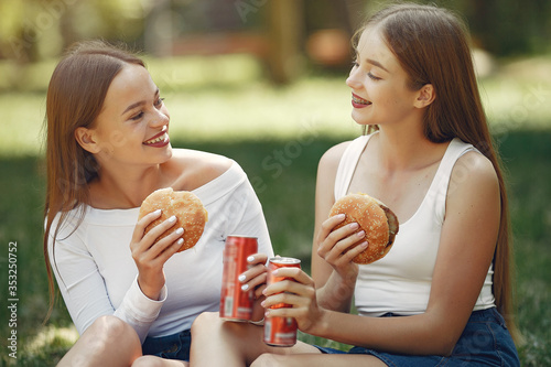 Beautiful girls in a jeans skirts. Women in a summer park. Friends with a burgers