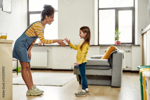Nice to meet you. African american woman baby sitter get acquainted with caucasian cute little girl. They are standing indoors and talking photo