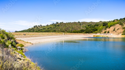 Stevens Creek reservoir on a sunny day, with people walking and relaxing on the dam and shoreline; south San Francisco bay area, California