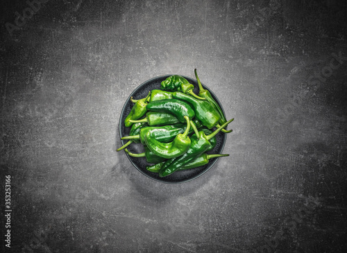 Bowl of fresh green peppers on grey background. Overhead shot with copy space.