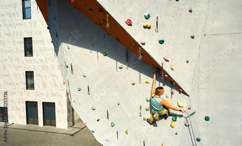 Active sporty woman practicing rock climbing on artificial rock wall in climbing gym. Athletic girl reaching holds, making hard move and gripping hold. Conquering, overcoming and active lifestyle