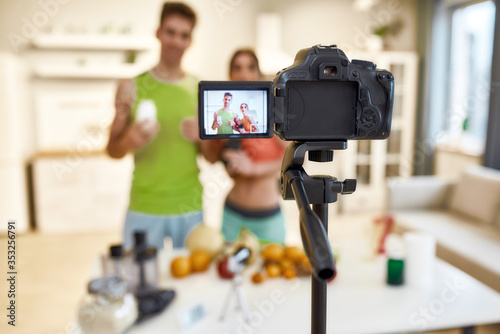 Capturing ideas for Life. Young couple recording video blog or vlog about their nutrition on camera at home. Man and woman showing vitamins and supplements standing in the kitchen