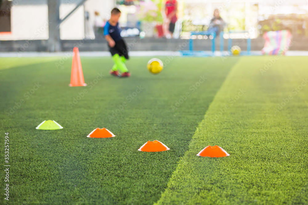selective focus to marker cones are soccer training equipment on green artificial turf with blurry kid players training background. material for training class of football academy. selective focus to marker cones are soccer training equipment on green artificial turf with blurry kid players training background. material for training class of football academy.