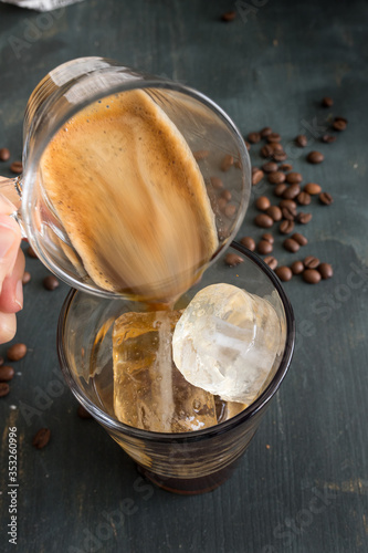 Coffee glass being dropped into a coffee cup full of ice cubes.
