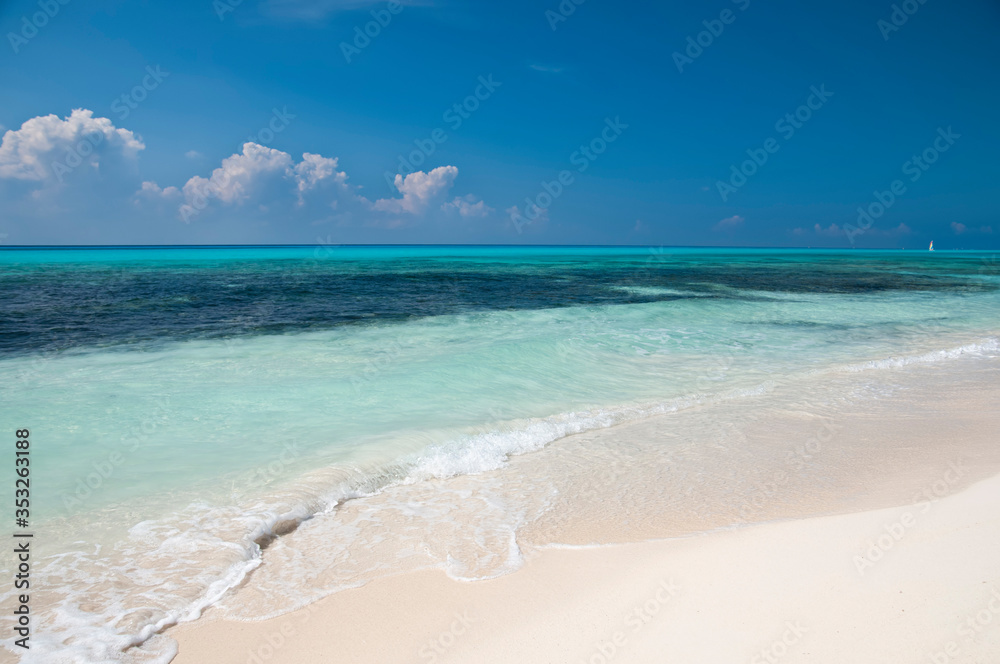 Deserted and paradisiacal Caribbean beach, with a calm and turquoise sea, with a sailboat that sails to the horizon