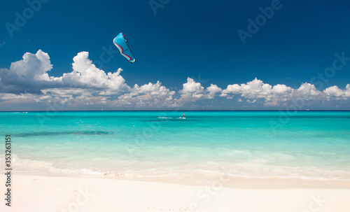 Kitesurfer with Kiteboard in front of an amazing and deserted tropical beach, on the horizon the blue sky and white clouds