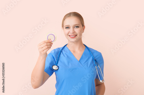 Female gynecologist with condom on color background