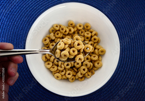 breakfast cereal in a spoon over a white bowl on a blue placemat