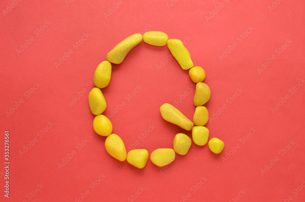 Letter Q made of old Yellow pebbles on a red background