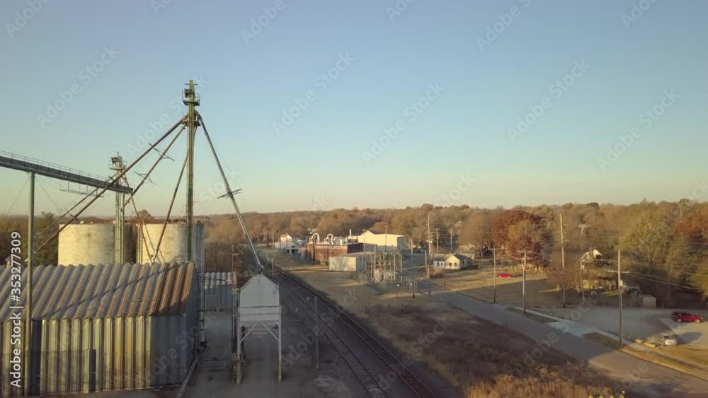 Aerial view of Industrial facility by railroad tracks rising above to reveal rural American town and landscape Aerial view of Industrial facility by railroad tracks rising above to reveal rural American town and landscape