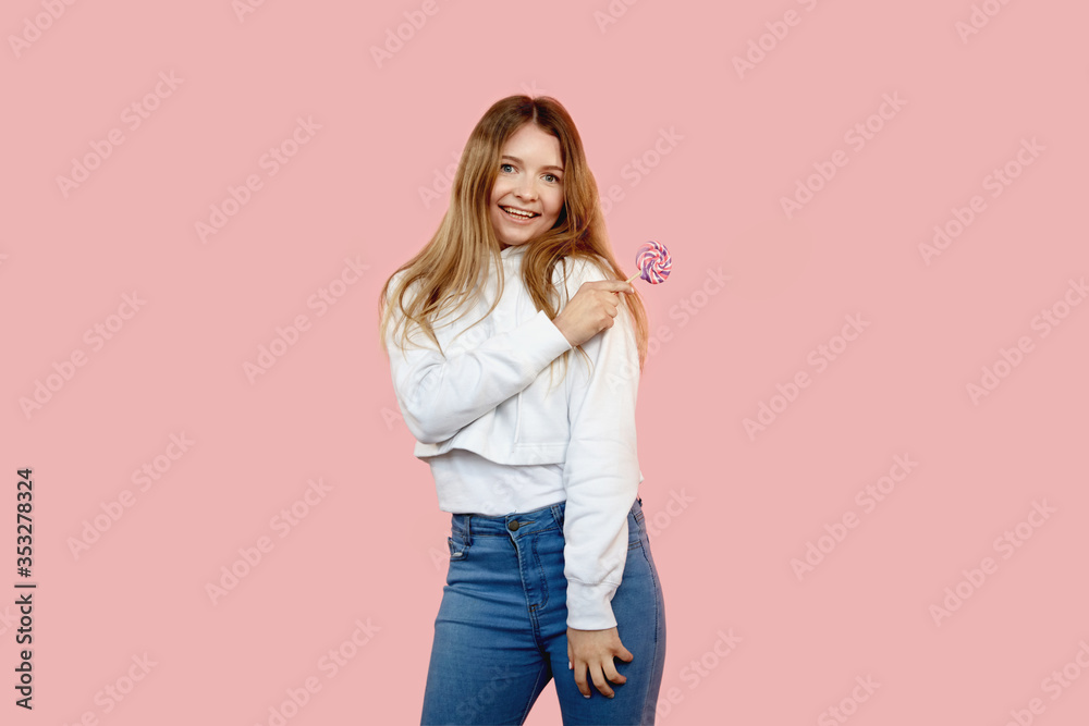 The funny girl up in jeans with a lollipop smiling and looking at the camera The funny girl up in jeans with a lollipop smiling and looking at the camera