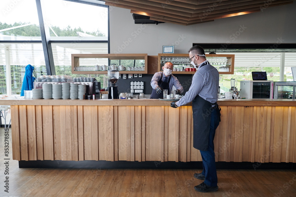 waiter in a medical protective mask serves the coffee in restaurant waiter in a medical protective mask serves the coffee in restaurant
