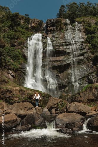 A vertical shot of a woman standing in front of waterfall in the jungle. View from back, explore beautiful places of the world photo