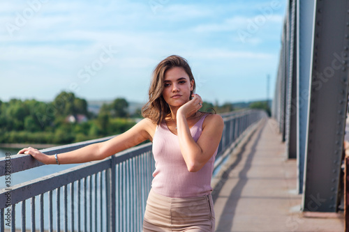 Fototapeta Naklejka Na Ścianę i Meble -  Pretty young woman posing on the old rusty transport bridge over the river during sunset.