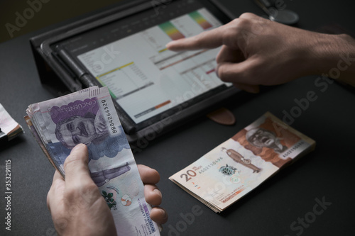 a man's hand holding Colombian bills while he does the math on a tablet
