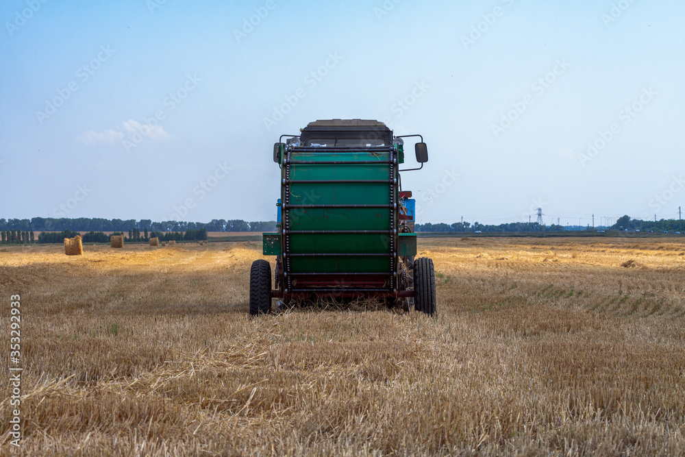 Obraz premium tractor makes big straw roll on yellow field at summer day