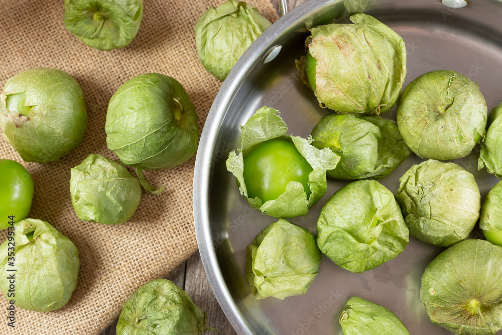 A top down view of tomatillos on burlap material and inside a steel saucepan, in a still life setting. A top down view of tomatillos on burlap material and inside a steel saucepan, in a still life setting.
