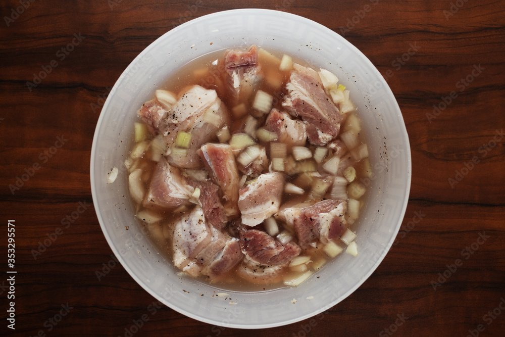 Pork brisket barbecue marinade before cooking with pieces of meat and spices in a bowl on a wooden background