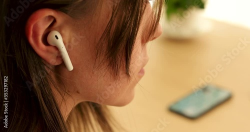 Woman inserts a wireless white earphone into her ear close-up
