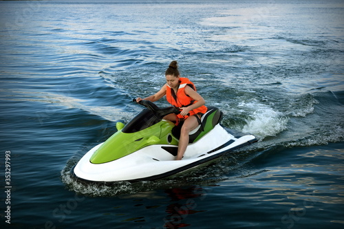 A young woman in a life jacket rides a water bike on a lake in summer.
