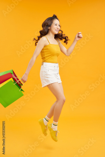 Joyful Teen Summer Girl Carrying Shopping Bags And Jumping In Air Over orange Background, Full-Length Shot With Copy Space