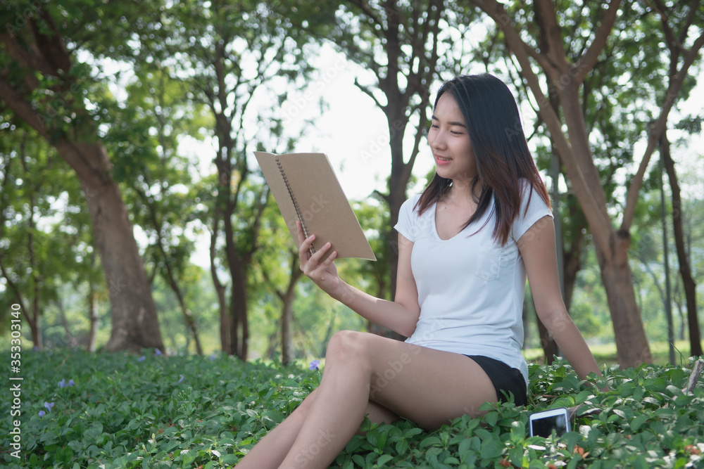 Digital detox concept. Asian beautiful woman reading a book by not use smartphone for relaxing activity without digital technology in the park on natural light freshness morning Digital detox concept. Asian beautiful woman reading a book by not use smartphone for relaxing activity without digital technology in the park on natural light freshness morning
