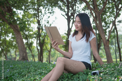 Digital detox concept. Asian beautiful woman reading a book by not use smartphone for relaxing activity without digital technology in the park on natural light freshness morning