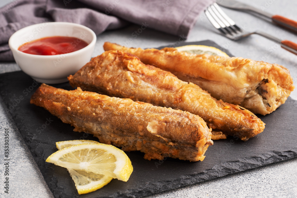 Fried fish hake Pollock with tomato sauce and slices of fresh lemon. Concept eating fatty fast food. Grey concrete background copy space.