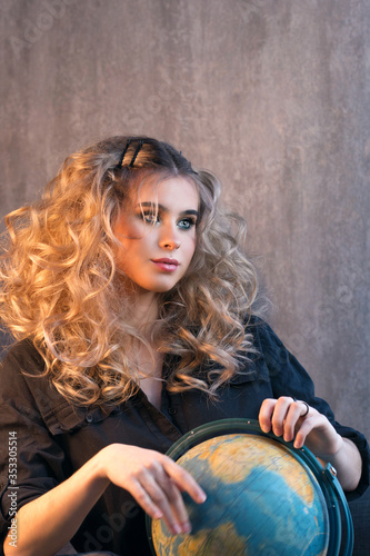 Blonde girl with long and volume shiny wavy hair. Beautiful model woman with curly hairstyle. Holds a globe in his hands and rotates it. The concept of world travel and freedom of movement