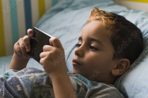 Little kid playing game on smartphone chilling on bed