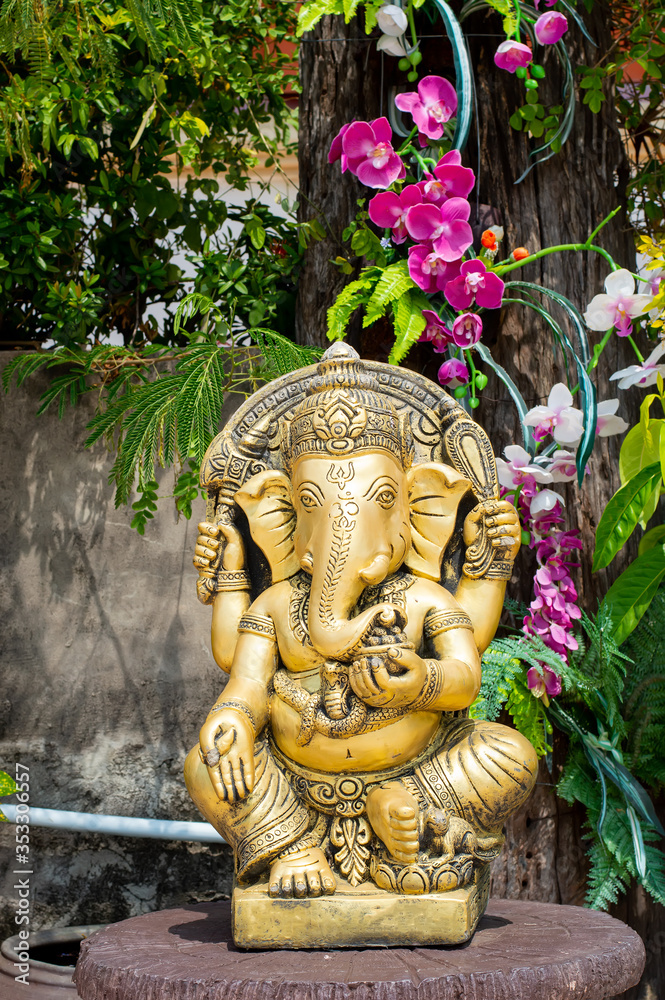 statue gold ganesha sitting under tree in garden orcid background