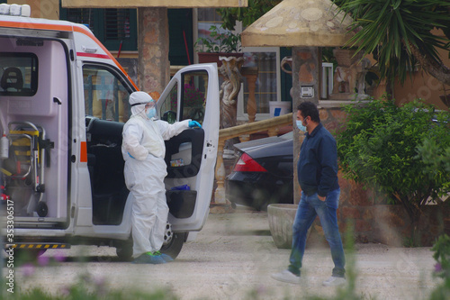  Home care operating unit with anti-Covid-19 or coronavirus protection at the service of a patient, in the meantime a pedestrian with a protective mask passes.