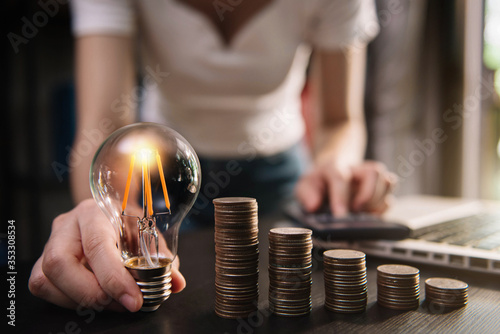 Business woman hand holding lightbulb with coins stack on desk. concept saving energy and money at office.
