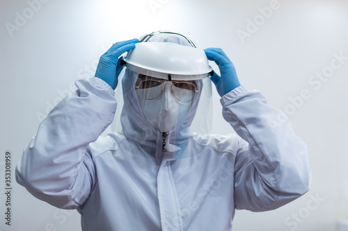Male doctor wearing white biosecurity suit, blue gloves, white mask and face shield photo