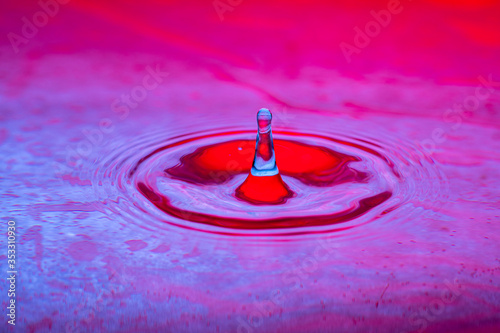splash of a drop of water on a color gradient burgundy violet surface close-up