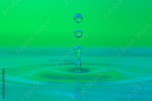 splash of water drop on a color gradient green surface close-up