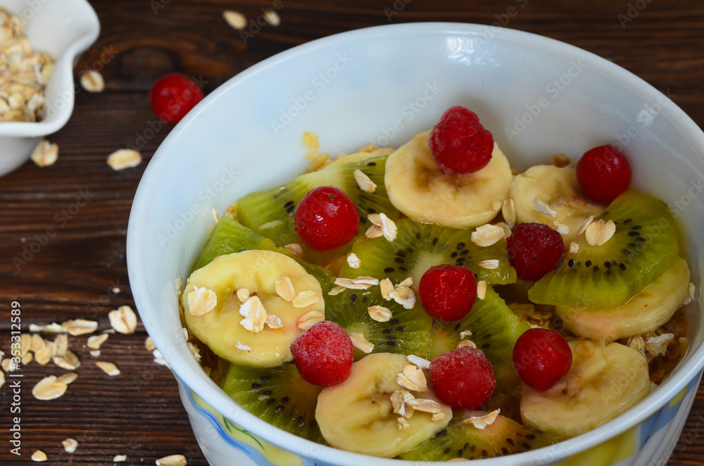 A rich and healthy breakfast. Oatmeal porridge with fruit and berries with kiwi banana and cherry. Diet concept. Natural and eco friendly food on a wooden table