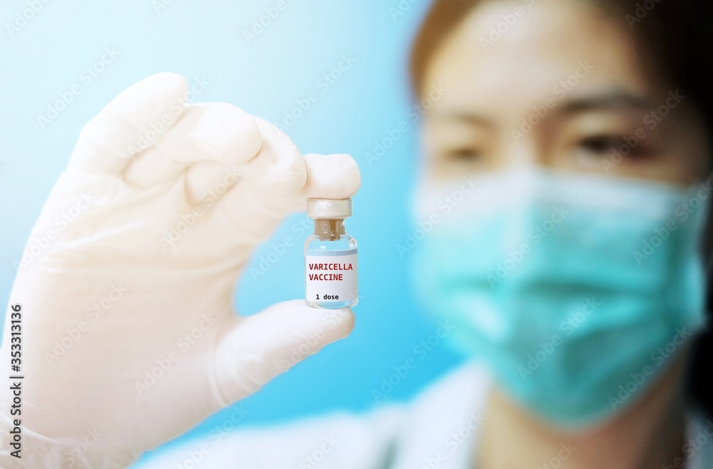 A female Asian physician with surgical mask and white rubber gloves at a clinic, holding a glass bottle of 1 dose Varicella or Chickenpox vaccine with white background and red letters.