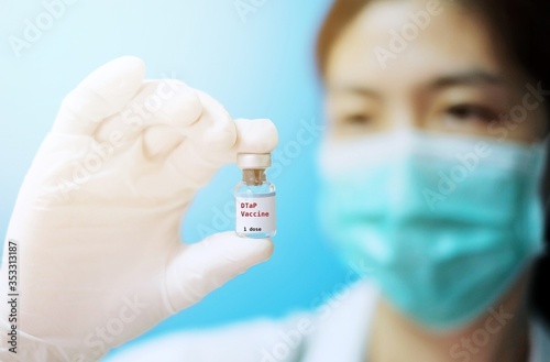 A female Asian physician with surgical mask and white rubber gloves at a clinic, holding a glass bottle of 1 dose DTaP or VIS vaccine, with white background and red letters.