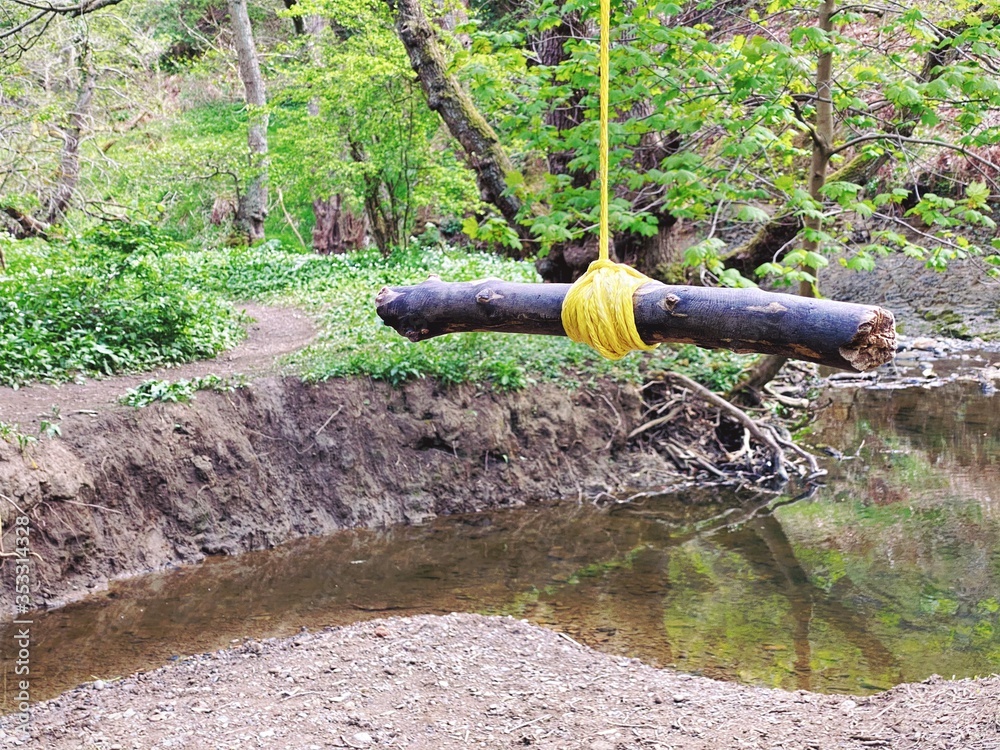 Close up details of a rope swing hanging from the branches of a mature tree in a forest. A small stick is tied with knot as a handle to swing over river below. Close up details of a rope swing hanging from the branches of a mature tree in a forest. A small stick is tied with knot as a handle to swing over river below.
