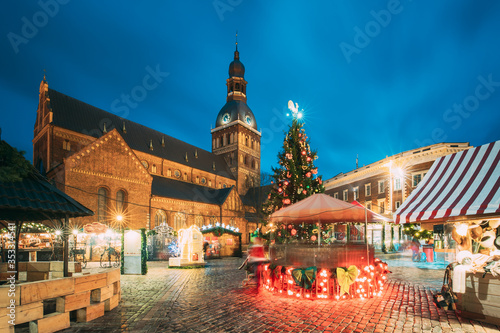 Riga, Latvia. Christmas Market On Dome Square With Riga Dome Cathedral. Christmas Tree And Trading Houses. Famous Landmark At Winter Evening Night In Illuminations Light © Grigory Bruev