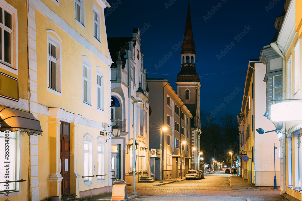 Fototapeta premium Parnu, Estonia. Night Nikolai Street With Old Houses, Restaurants, Cafe, Hotels And Shops In Evening Night Illuminations. View Of Lutheran Church Of St. Elizabeth On Background