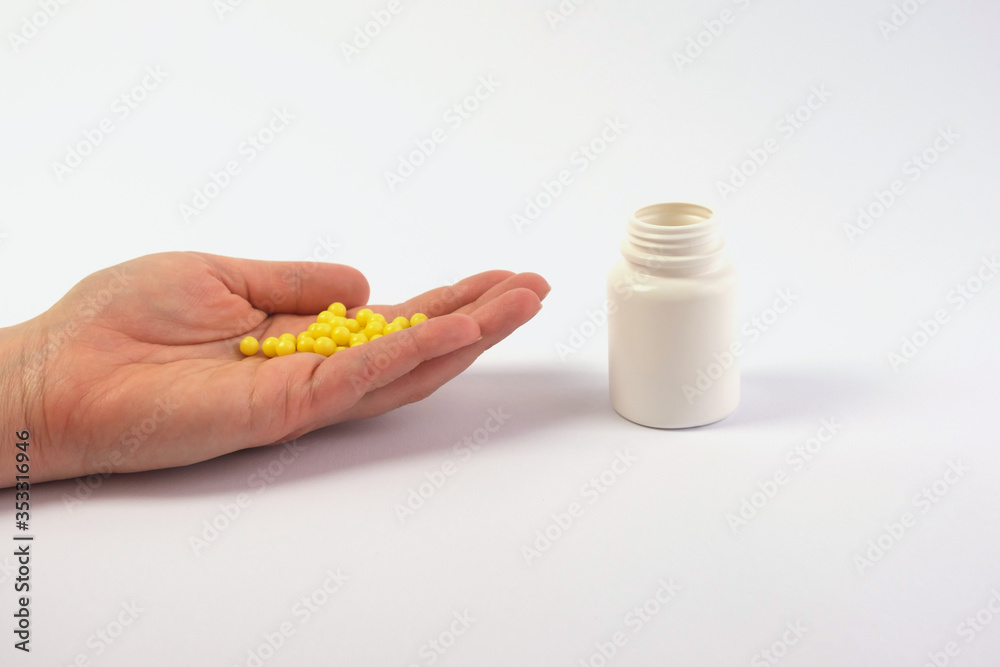 Obraz premium Hand with pills, pills, vitamins and an adjacent white jar. The purpose of treatment, medications, vitamins. Taking painkillers. Copy space
