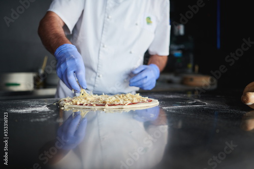 chef with protective coronavirus face mask preparing pizza